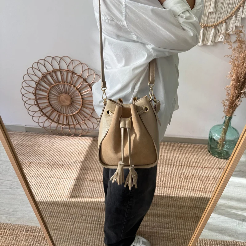 Bolso bucket combinado serraje y piel taupe pompón iniciales bordadas