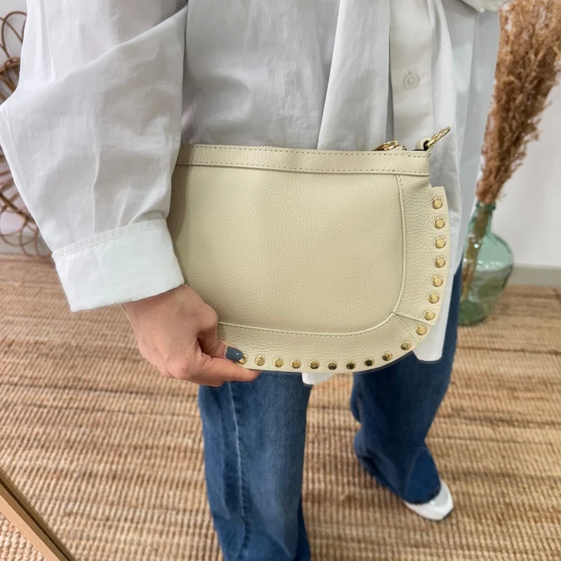 Bandolera ovalada piel tachuelas beige iniciales bordadas