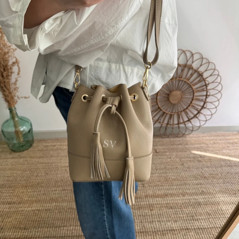 Bolso bucket piel taupe pompón iniciales bordadas