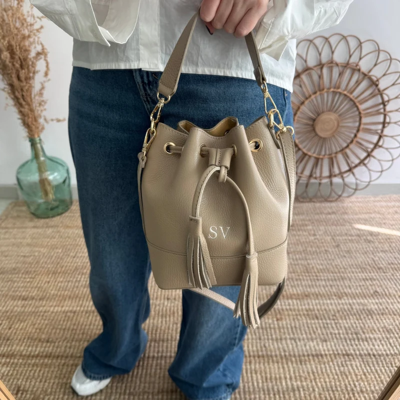 Bolso bucket piel taupe pompón iniciales bordadas