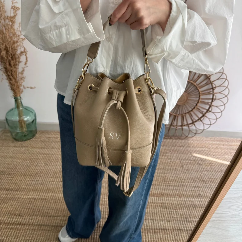 Bolso bucket piel taupe pompón iniciales bordadas